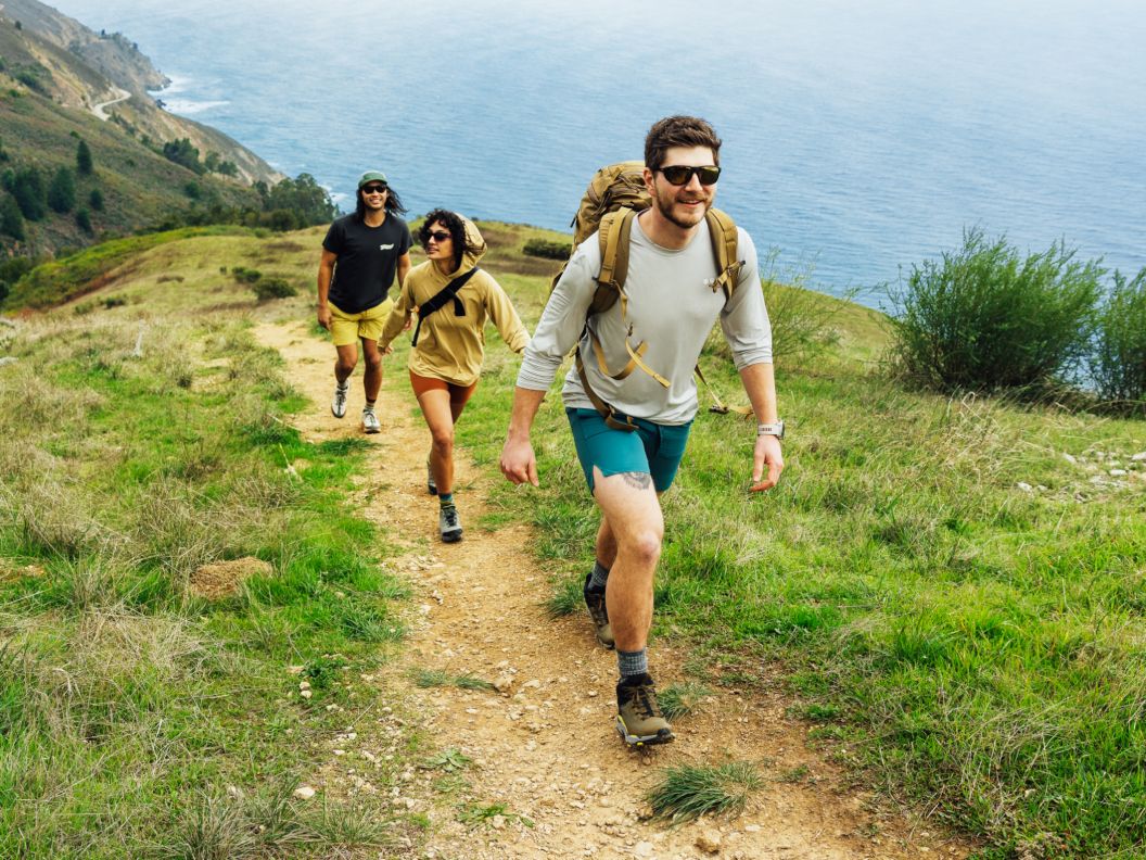3 people hike up a trail near the ocean.